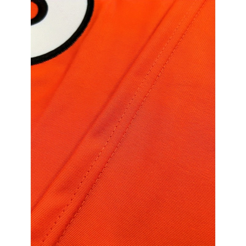Close-up of an orange fabric surface of Custom Men's Orange Football Jersey – Cincinnati Fan Gameday Gear with visible stitching and part of a white circular graphic with black detailing at the top left.