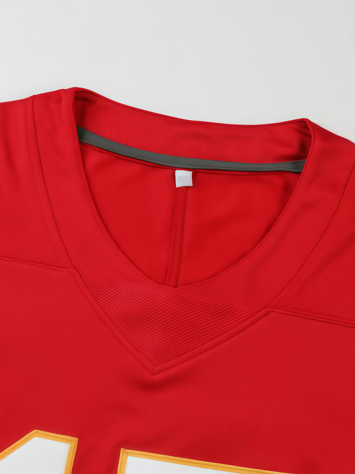 Close-up of a red  Red Football Jersey – Kansas City Fan Gameday Gear for men with a V-neck collar, showing a gray inner neck trim and part of a white-and-gold number graphic at the bottom.