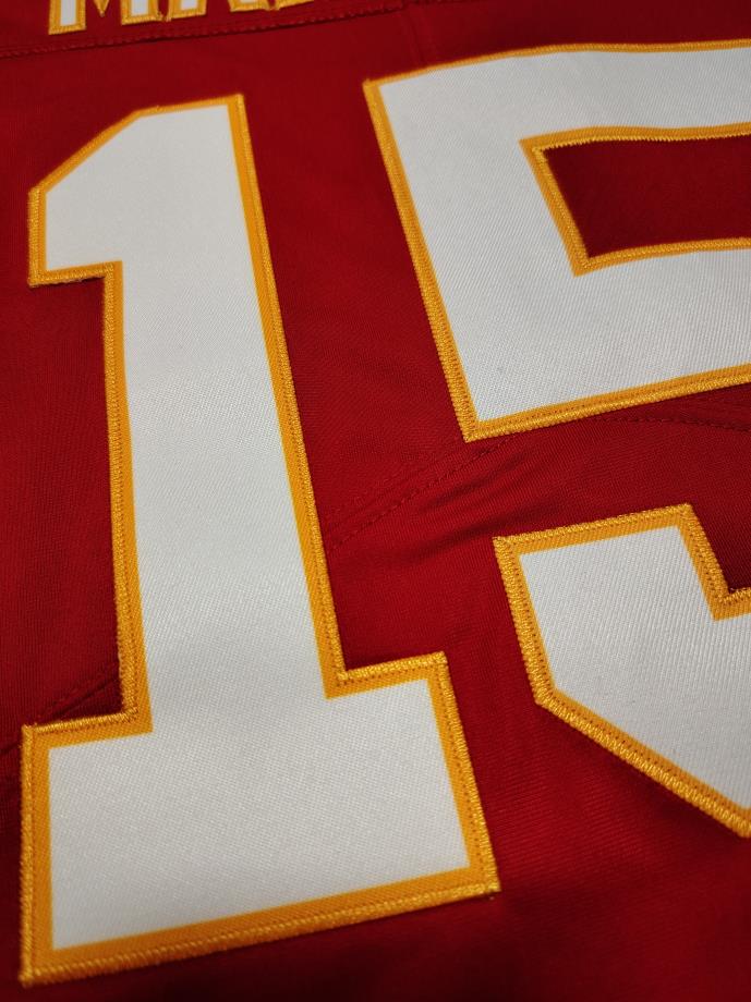 Close-up of a red football jersey with large white number 15 outlined in gold/yellow embroidery.